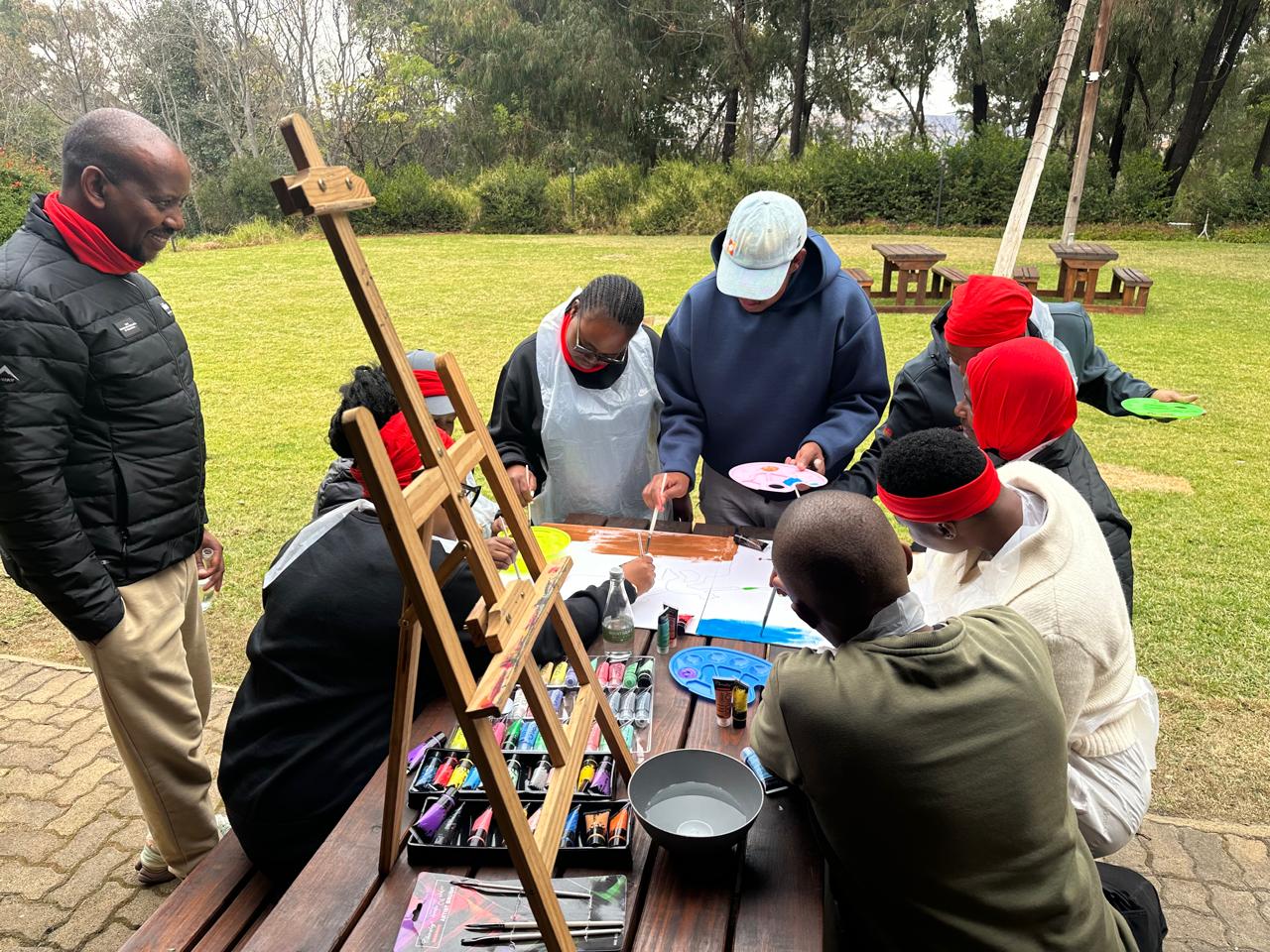 Teams painting a large collaborative artwork on easels outdoors